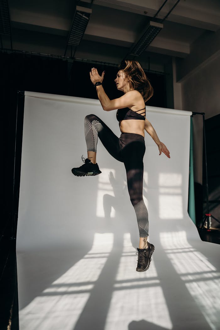 Dynamic shot of a woman in activewear jumping in a studio, showcasing fitness and energy.